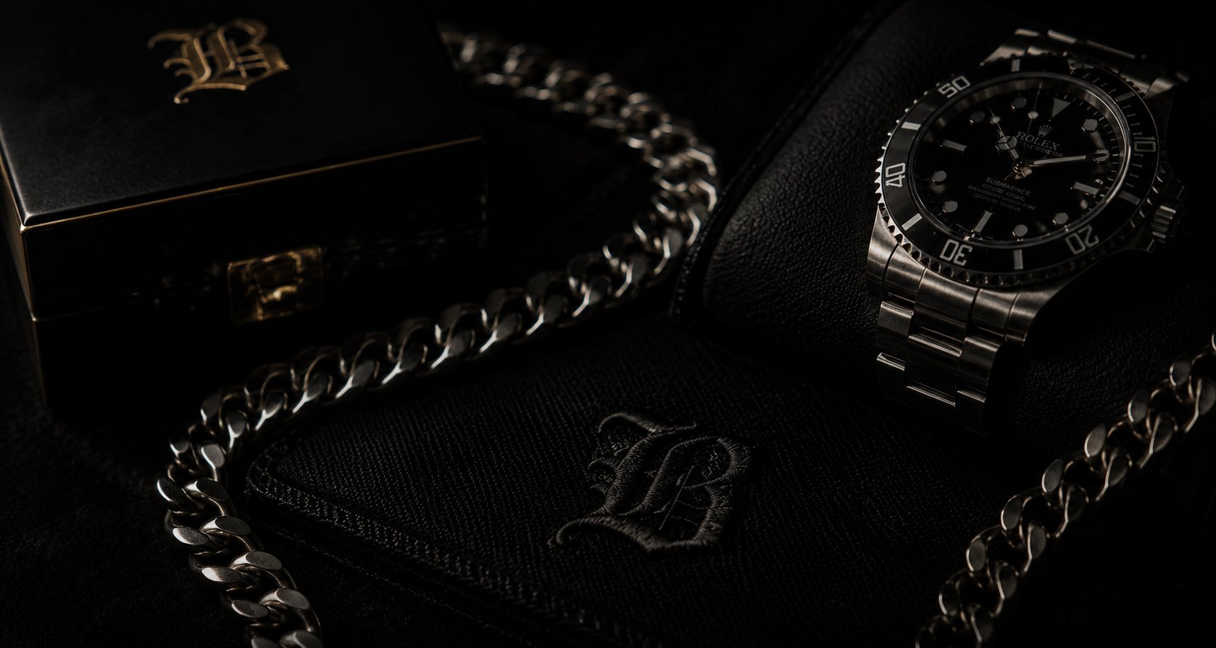 Luxury watch and silver chain bracelets on black wallet with gold emblem, stylish accessories flatlay