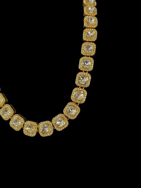 Gold diamond tennis necklace with square cushion-cut stones arranged in a U-shape on black background
