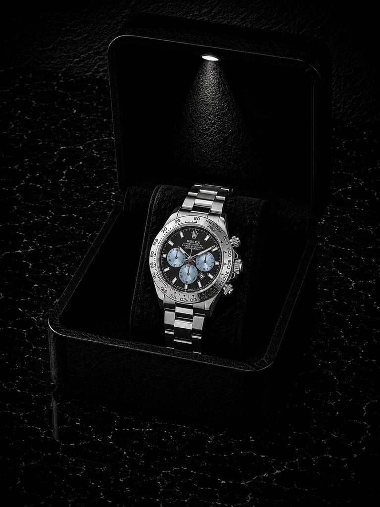 Luxury stainless steel chronograph watch with blue dial displayed in open black presentation box with spotlight lighting against textured dark background