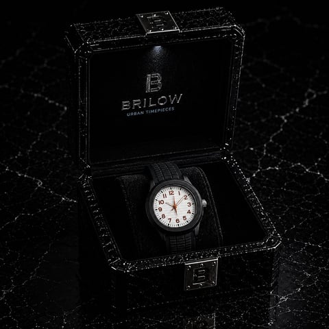 Brilow brand watch with white face and dark band displayed in open black luxury box against textured dark surface