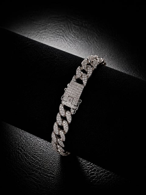 Diamond-encrusted Cuban link chain bracelet with rectangular clasp on black textured surface