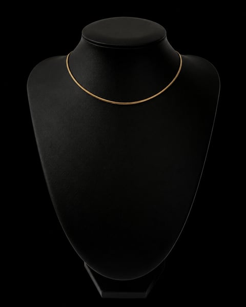 Gold snake chain necklace displayed on black mannequin bust against dark background