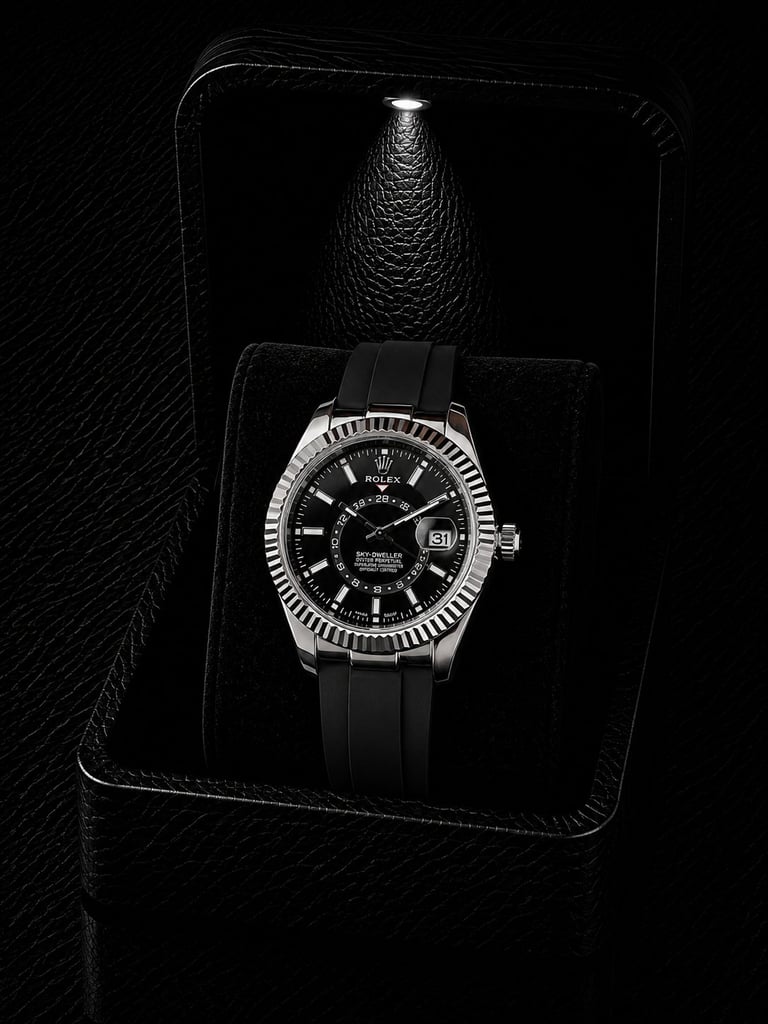 Luxury watch with silver bezel and black dial displayed on black leather in dramatic lighting