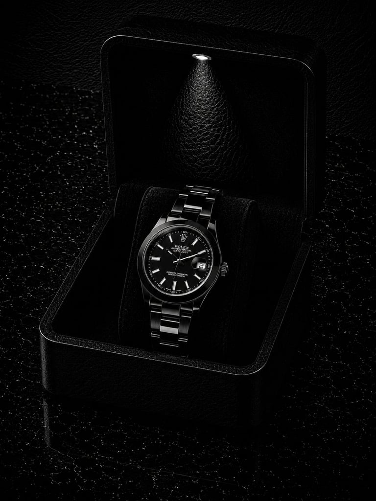 Luxury stainless steel wristwatch with black dial displayed in open black leather box on dark textured surface.