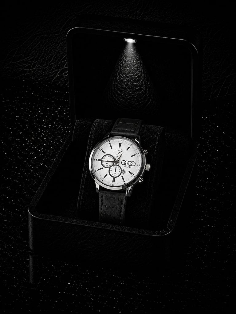 Luxury chronograph wristwatch with white dial and black leather strap displayed in black presentation box with dramatic lighting