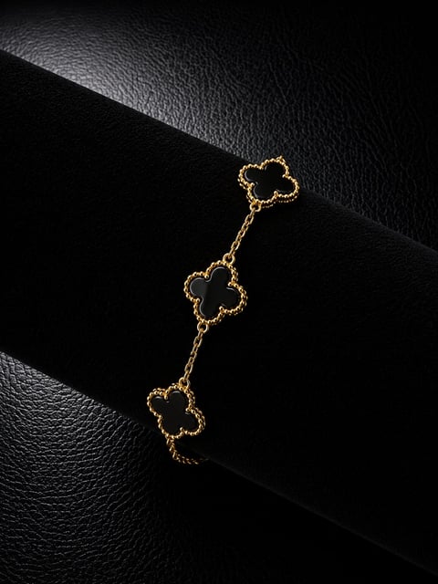 Gold clover-shaped charm bracelet with three leaf motifs arranged diagonally on black textured leather background