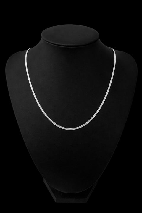 Silver chain necklace displayed on a black velvet jewelry bust form against a dark background